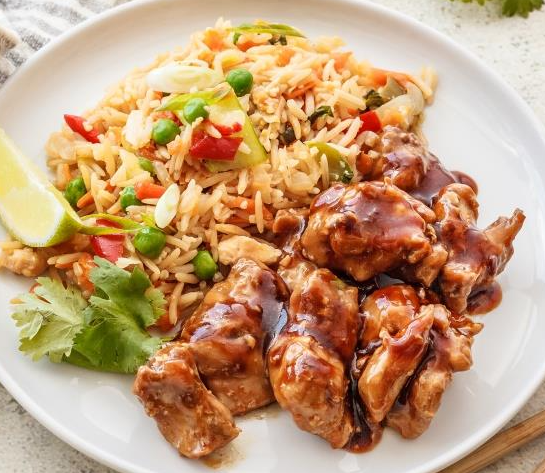 Plate with glazed chicken, fried rice with peas, red peppers, lime wedge, and cilantro.
