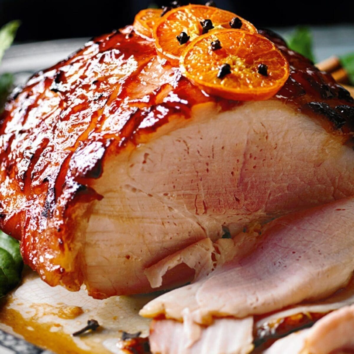 Glazed ham with orange slices and cloves, partially sliced to show juicy interior.
