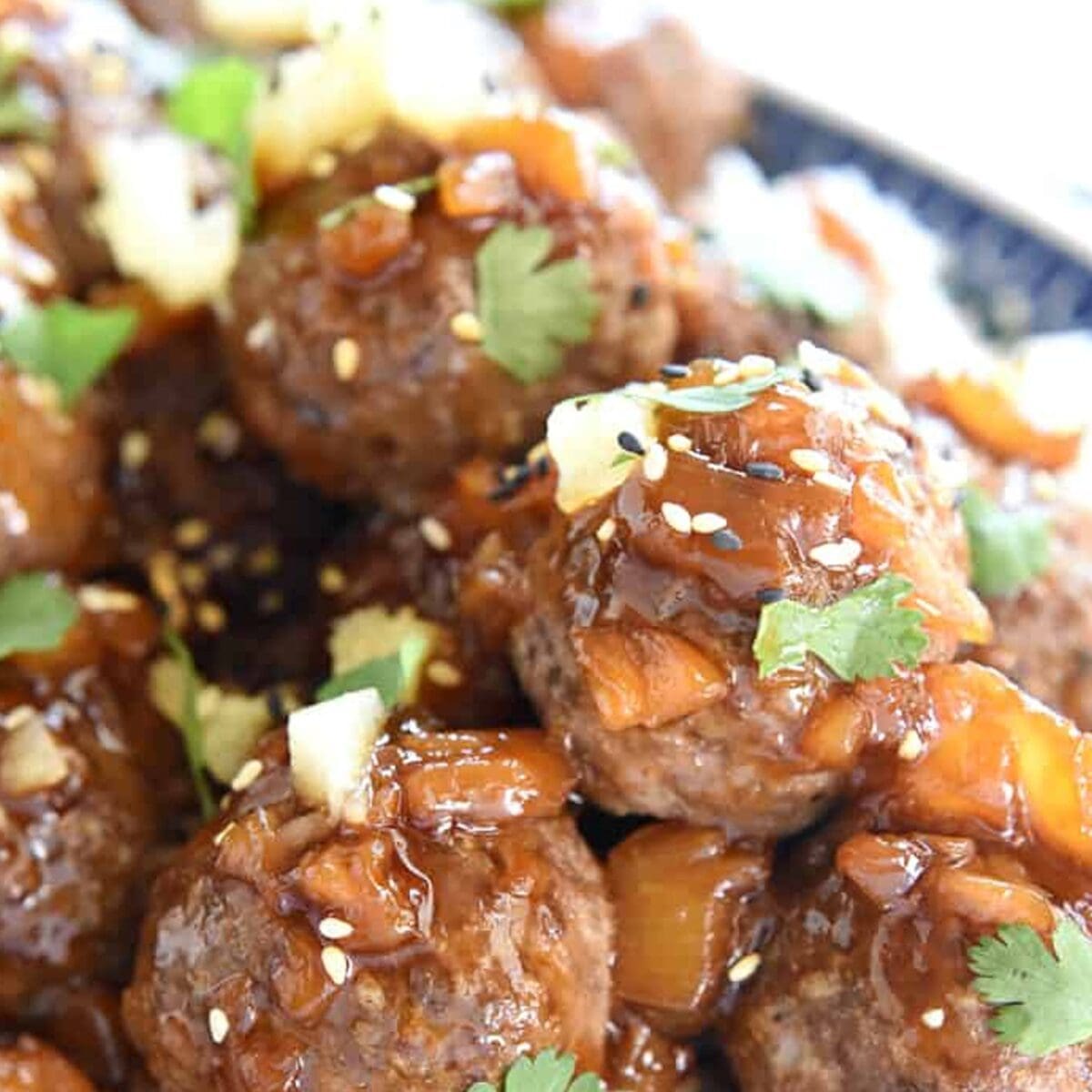 Glazed meatballs with herbs, pineapple, and sesame seeds in a rich sauce served in a bowl.