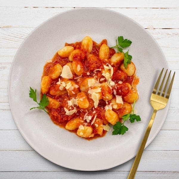 Gnocchi with tomato sauce, Parmesan, parsley on plate; gold fork on white wooden table.