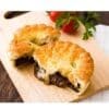 Golden pastry pie with dark filling on a board, tomatoes and parsley in the background.