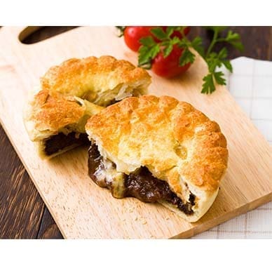 Golden pastry pie with dark filling on a board, tomatoes and parsley in the background.
