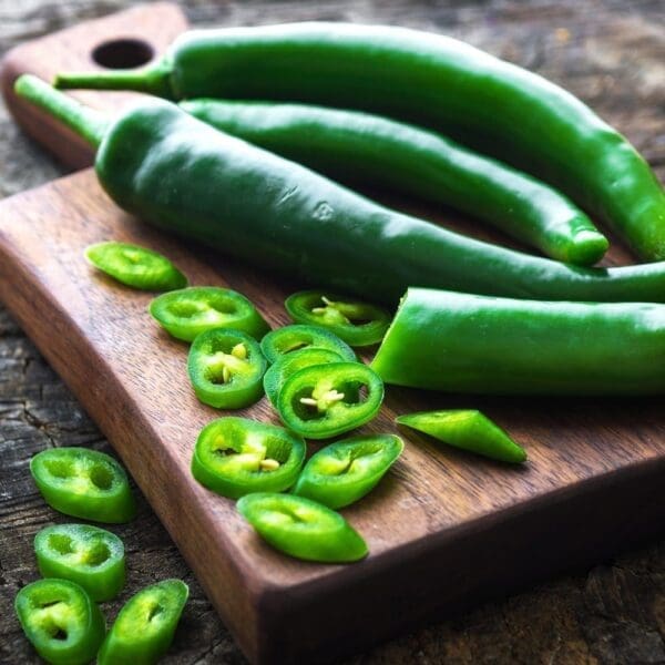 Green chili peppers, whole and sliced, on a wooden cutting board with visible seeds.