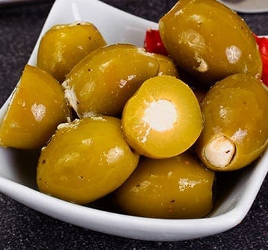 White dish with green olives and red pepper pieces. Some olives are stuffed with white filling.
