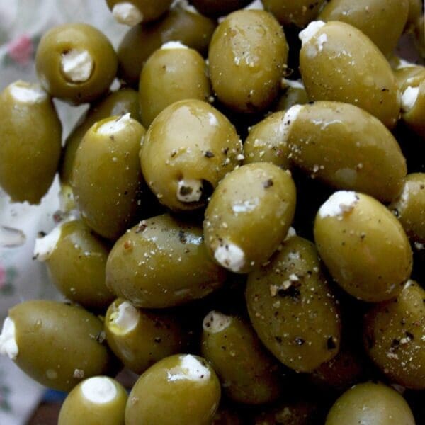 Close-up of green olives stuffed with white cheese, sprinkled with ground black pepper.