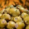 Bowl of glossy green olives stuffed with herbs and meat against a warm blurred background.