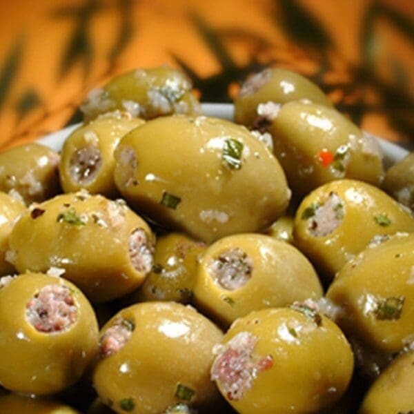 Bowl of glossy green olives stuffed with herbs and meat against a warm blurred background.
