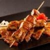 Skewered grilled chicken with glazed sauce, grilled vegetables, and pickled garnish.