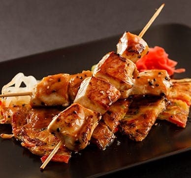 Skewered grilled chicken with glazed sauce, grilled vegetables, and pickled garnish.