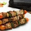 Grilled meat skewers with bell peppers, tomatoes, and onions on a plate near a grill pan.