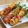 Grilled meat skewers with herbs and red pepper flakes on a white plate, wicker placemat background.