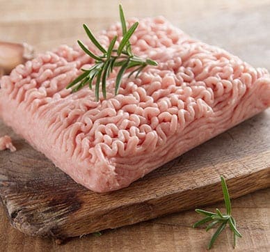Ground turkey on a wooden board with rosemary and garlic in view.