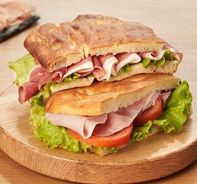 Sandwich with ham, lettuce, and tomato on toasted bread on a round wooden serving board.