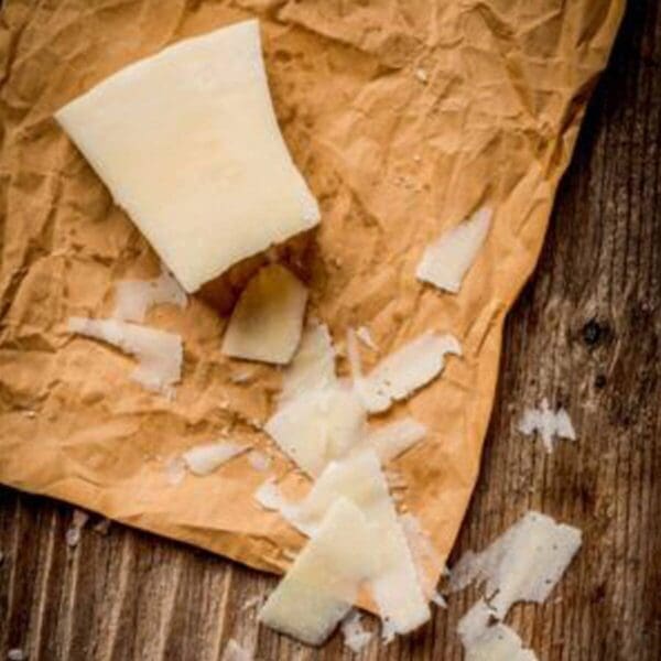 Hard cheese on crinkled paper with shavings, resting on a wooden surface.