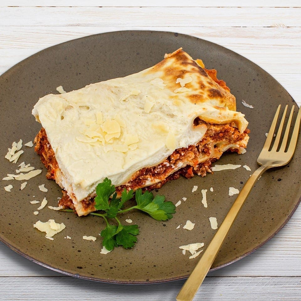 Plate of lasagna with layers, cheese, parsley, and golden fork on wooden background.