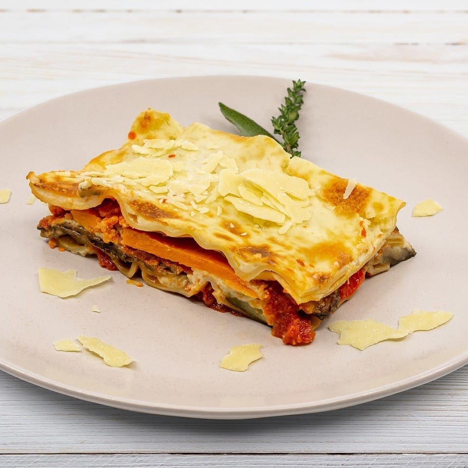 Lasagna slice on beige plate with cheese, pasta, tomato sauce, vegetables, and herbs.