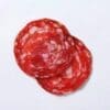 Two slices of marbled salami with red meat and white fat on a plain background.