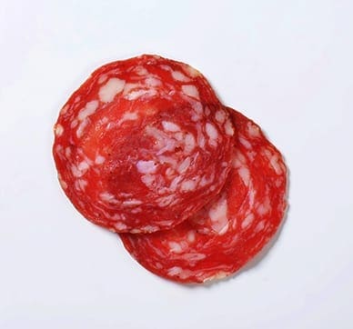 Two slices of marbled salami with red meat and white fat on a plain background.
