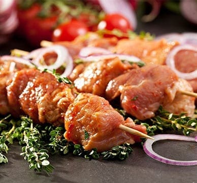 Marinated meat skewers with fresh herbs, sliced red onions, and blurred cherry tomatoes.