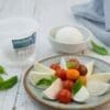 Plate with mozzarella slices, cherry tomatoes, basil; container and bowl in background.