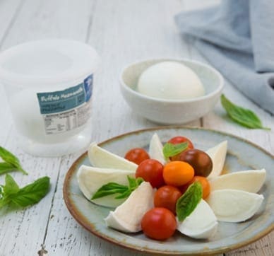 Plate with mozzarella slices, cherry tomatoes, basil; container and bowl in background.