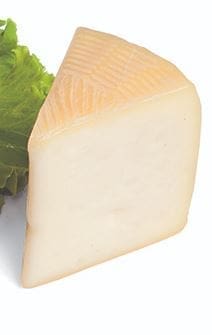 Wedge of pale cheese with textured rind on green lettuce background.