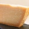 Wedge of pale yellow hard cheese with rough texture on dark slate surface.