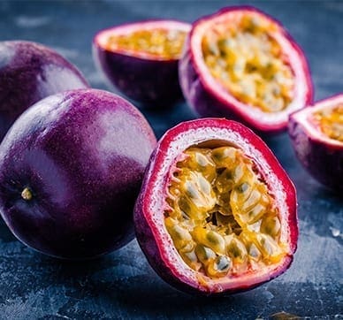 Passion fruits on dark surface, some whole with purple skins, others halved showing yellow interiors.