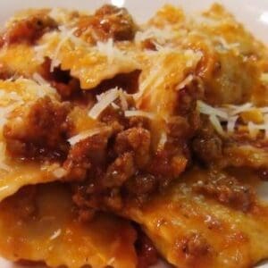 Plate of ravioli with meat sauce and grated cheese garnish.