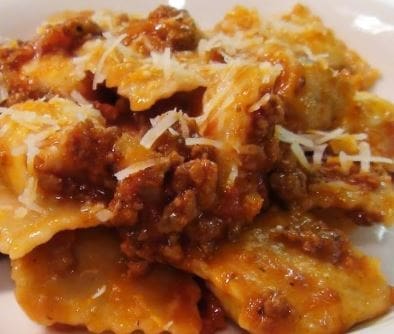 Plate of ravioli with meat sauce and grated cheese garnish.