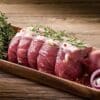 Slices of raw beef with rosemary, garlic, herbs, and red onion on a wooden tray.