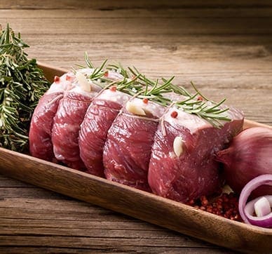 Slices of raw beef with rosemary, garlic, herbs, and red onion on a wooden tray.