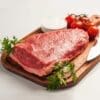 Raw beef on cutting board with tomatoes, salt, parsley, and knife nearby.
