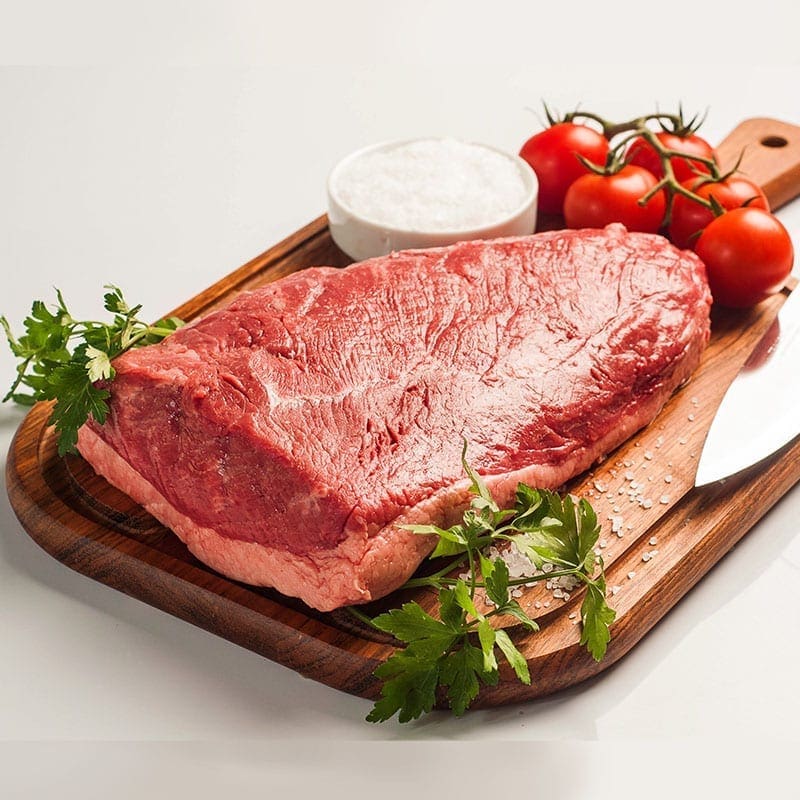 Raw beef on cutting board with tomatoes, salt, parsley, and knife nearby.