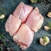 Four raw chicken breasts with garlic cloves and herbs on a dark surface.