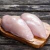 Raw chicken breasts on a wooden board with rustic wooden background.