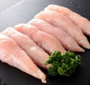 Slate platter with six raw chicken fillets and parsley garnish on dark background.