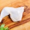 Raw chicken leg quarter on a wooden cutting board with fresh herbs.