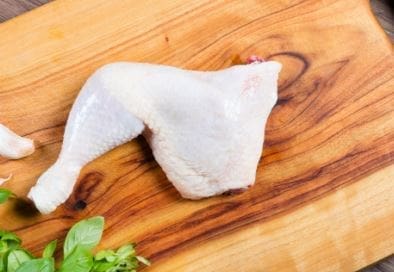 Raw chicken leg quarter on a wooden cutting board with fresh herbs.