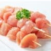 Raw chicken skewers topped with parsley on a white surface.