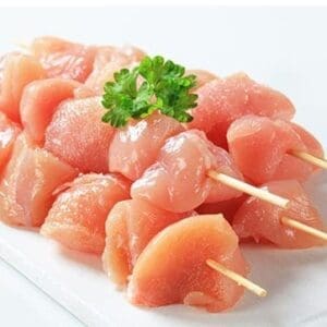 Raw chicken skewers topped with parsley on a white surface.