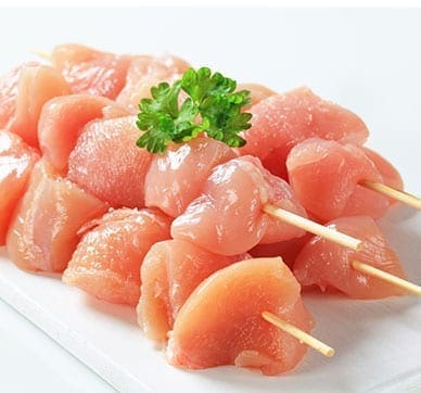 Raw chicken skewers topped with parsley on a white surface.
