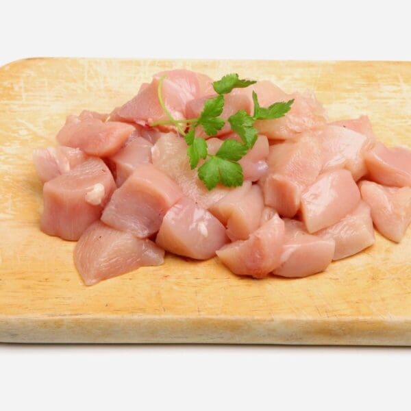 Raw cubed chicken breast on a wooden board with parsley garnish.
