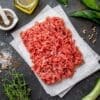 Raw ground meat on parchment paper with herbs, pepper, olive oil, salt, and bay leaves.