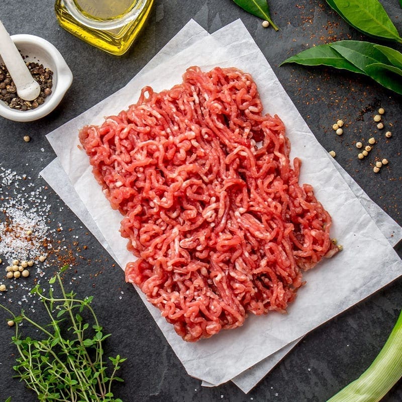 Raw ground meat on parchment paper with herbs, pepper, olive oil, salt, and bay leaves.