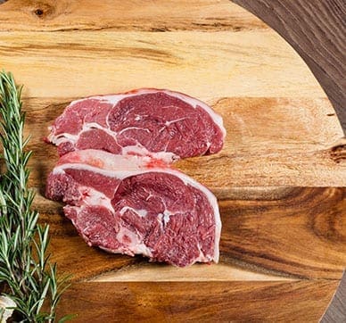 Two raw lamb chops on wooden board with fresh rosemary sprigs.
