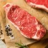 Raw marbled beef on parchment with peppercorns, coarse salt, and rosemary.