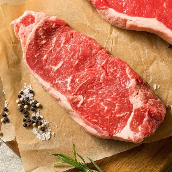Raw marbled beef on parchment with peppercorns, coarse salt, and rosemary.