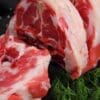 Raw marbled meat on dark surface, cut open; fresh dill, coarse salt, tomato in background.