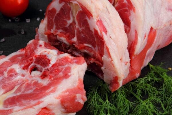 Raw marbled meat on dark surface, cut open; fresh dill, coarse salt, tomato in background.